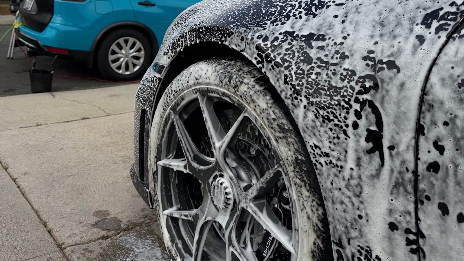 Close-up of a Porsche wheel and fender covered in foam during wheel and brake dust cleaning