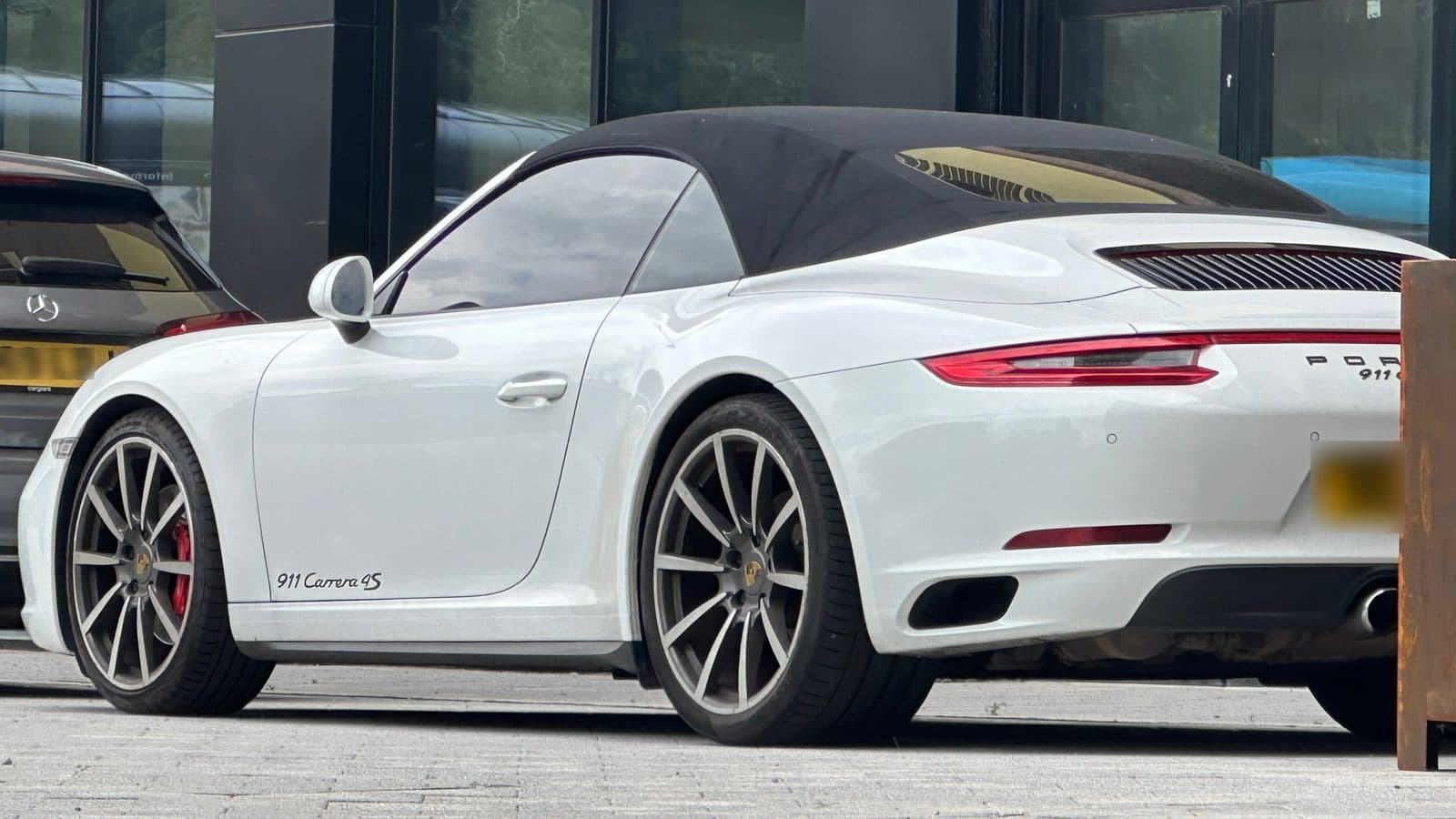 White Porsche 911 Carrera 4S Cabriolet with its black fabric soft top up, parked on the street