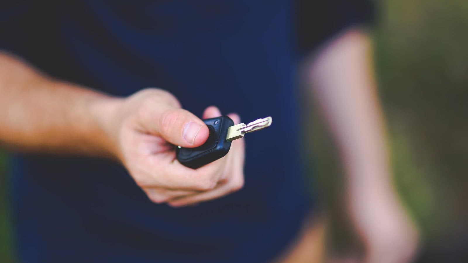 A hand holding out a car key fob, as when returning a leased car
