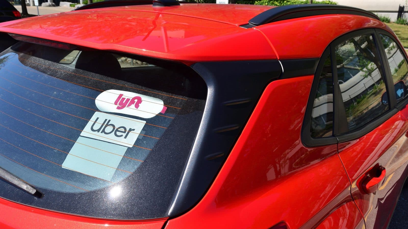 Rear window of a red hatchback displaying Uber and Lyft rideshare stickers