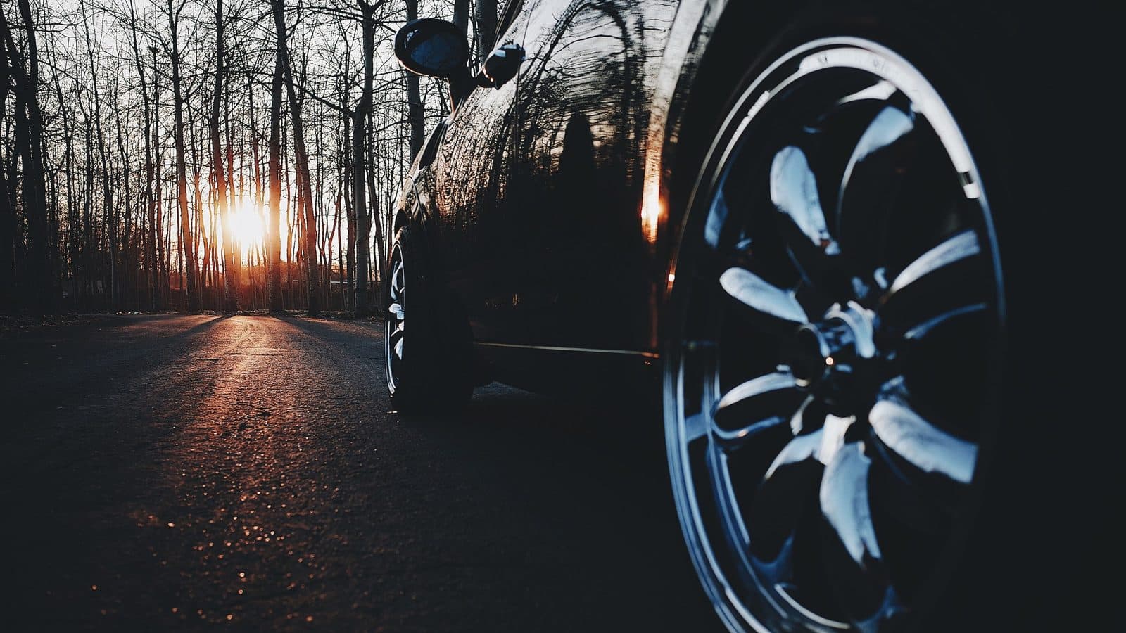 Glossy black car paint reflecting a sunset, the kind of dark finish where swirl marks show most