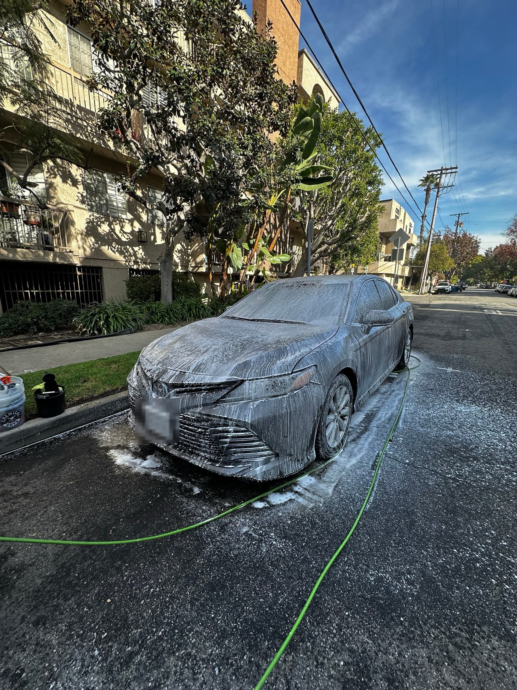 Toyota Camry covered in foam during the pre-wash stage on a residential street