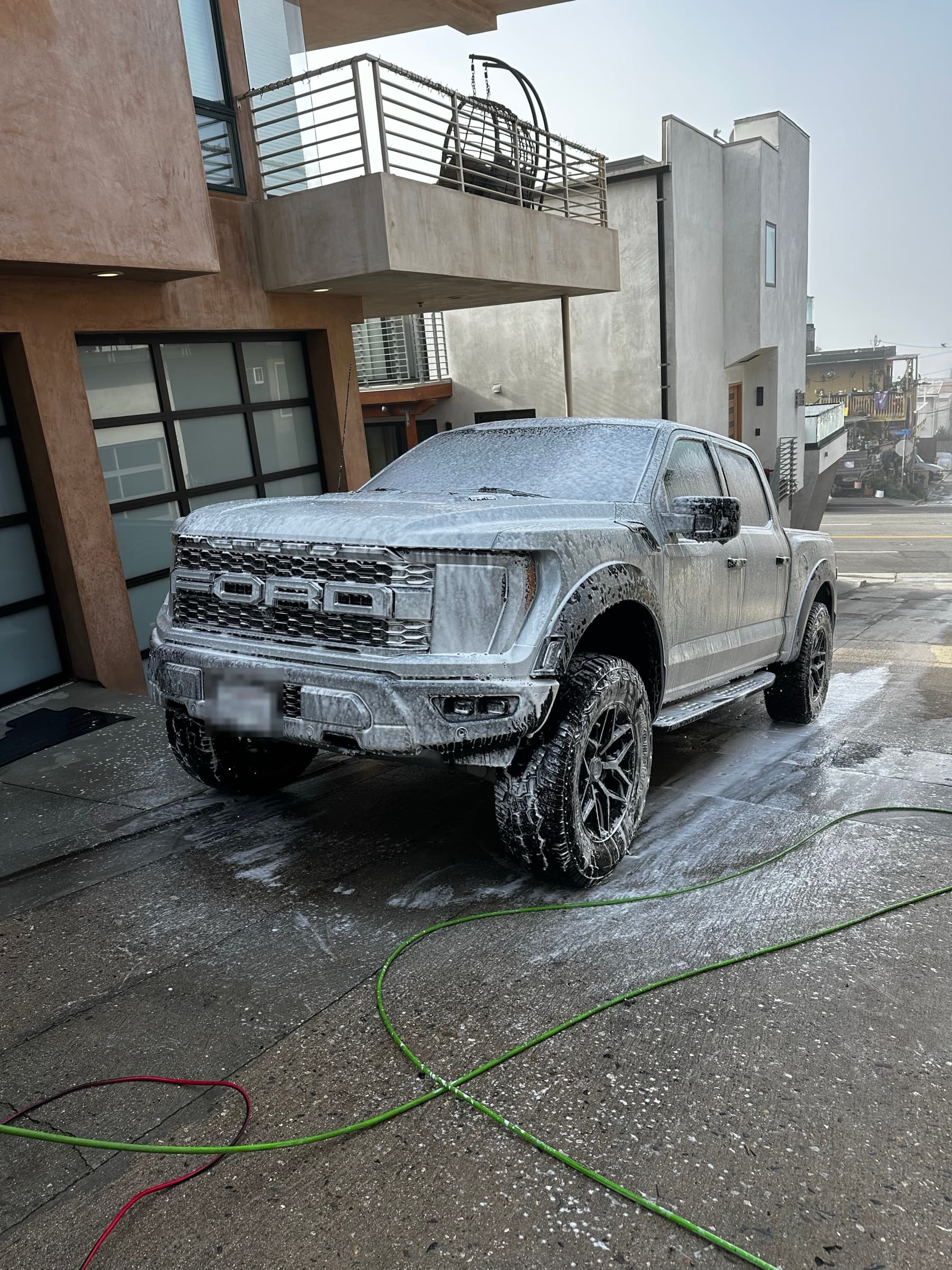 Ford Raptor truck covered in foam during the pre-wash stage in a driveway